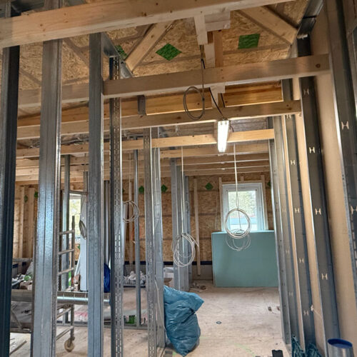 Baustelle eines Holzhauses mit sichtbaren Balken und elektrischen Kabeln.