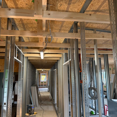 Baustelle mit Holzrahmen und Metallstreben, helle Beleuchtung, Kabel hängen herunter, unfertig.