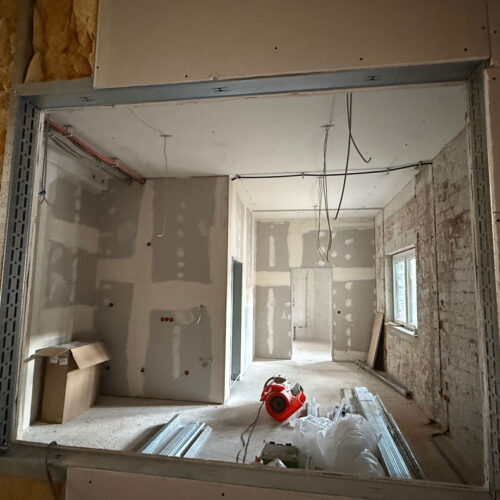 Baustelle mit unvollständigen Wänden, freiliegenden Kabeln und Baumaterialien auf dem Boden.