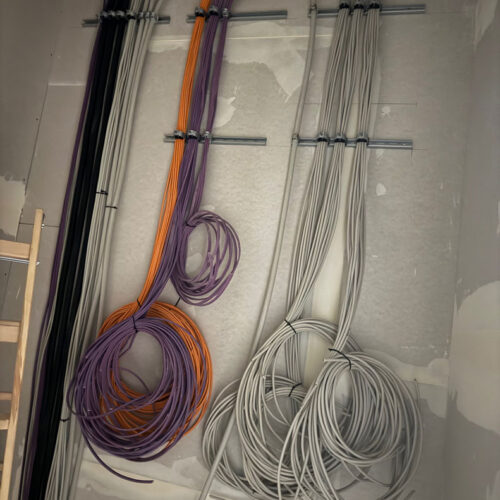 Alt-Text: Mehrere Kabelstränge an Wand befestigt, in Lila, Orange und Grau.