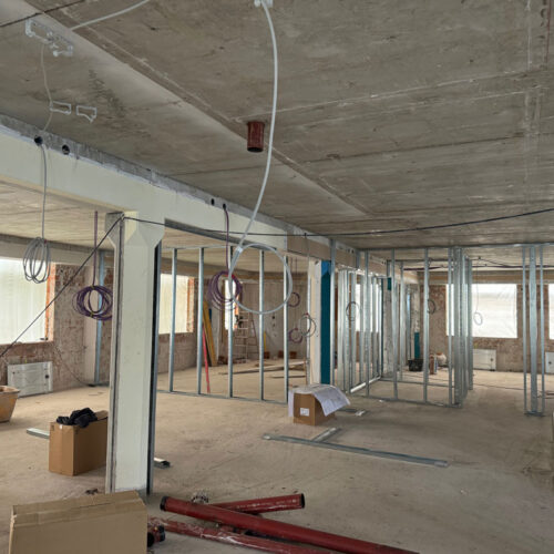Unvollständiger Bau mit Betonboden und -decke, Kabel hängen von der Decke, Metallrahmen sichtbar.