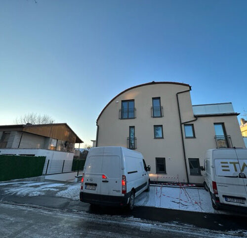 Ein modernes, beiges Gebäude mit zwei weißen Transportern davor bei klarem Himmel.