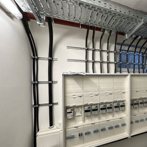 Elektroraum mit mehreren Schalttafeln und sorgfältig verlegten Kabeln an der Wand.