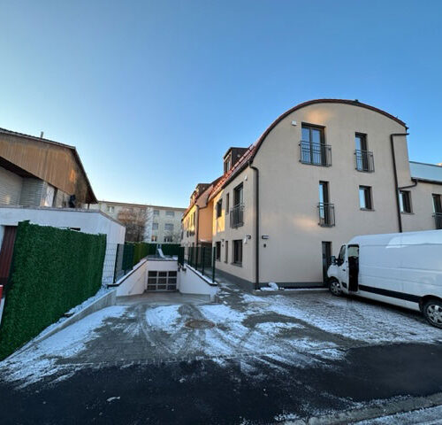 Mehrfamilienhaus im Winter, beige Fassade, blauer Himmel, weißer Lieferwagen im Vordergrund.
