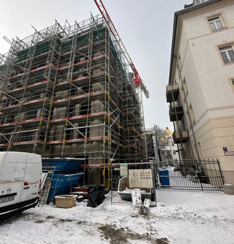 Baugerüst mit rotem Kran, verschneite Straße, weiße Gebäude, bewölkter Himmel.