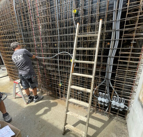 Zwei Bauarbeiter fokussiert an einer Metallkonstruktion, mit Leiter und grauen Arbeitskleidung.