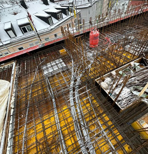 Verschneite Baustelle mit Stahlgerüsten, gelber Untergrund, Baukräne im Hintergrund.