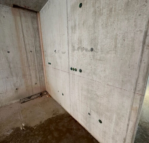 Betonwand mit Wasserstellen, sichtbaren Schraubenlöchern und glatter Oberfläche in einer Baustelle.