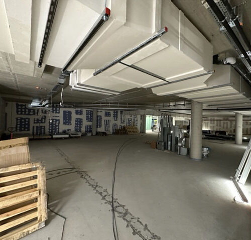 Ein leerer, unfertiger Raum mit Rohren an der Decke und Baumaterialien. Dim licht.
