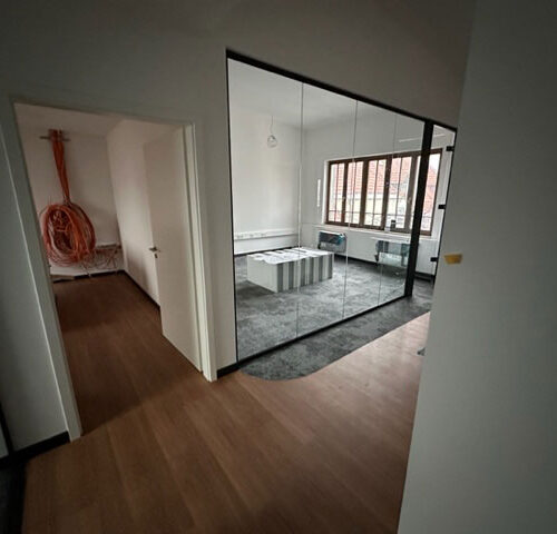 Büroinnenraum mit Glasschwingtüren, Holzboden, grauer Teppich, Kabelrolle an der Wand.