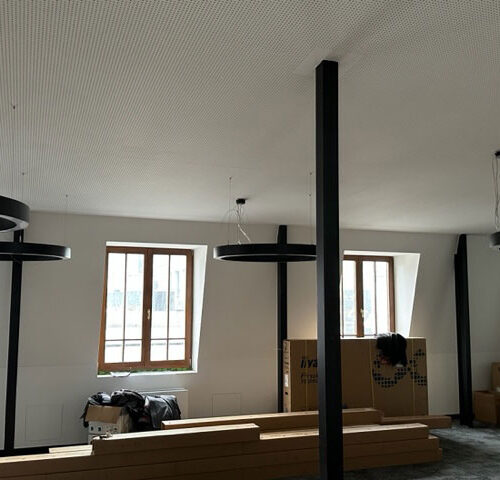 Ein leerer Raum im Bau, mit großen Fenstern, runden Leuchten und Kartons.