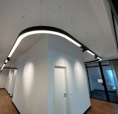Moderne Bürobeleuchtung mit geschwungenen LED-Leuchten an weißer Decke.