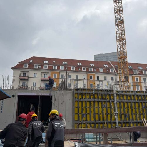 Bauarbeiter in Sicherheitskleidung arbeiten konzentriert an einer Baustelle vor einem mehrstöckigen Gebäude.