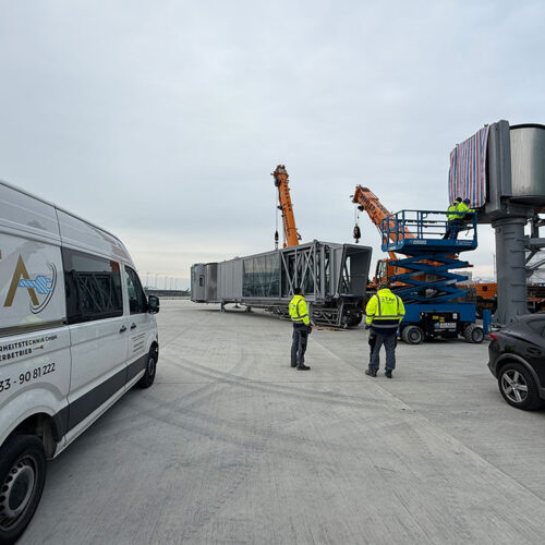 Mehrere Arbeiter in gelben Westen arbeiten mit Kranen an einer Flughafen-Gangway.