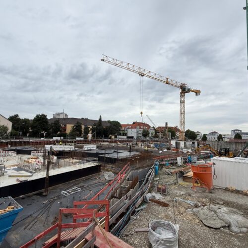 Eine Baustelle mit Baukränen unter bewölktem Himmel.