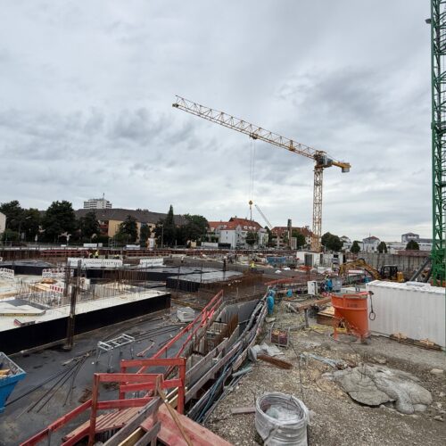 Eine Baustelle mit einem gelben Kran und grauem Himmel im Hintergrund.