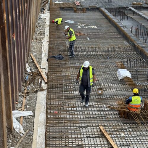 Mehrere Bauarbeiter in leuchtender Schutzkleidung arbeiten an einer Stahlkonstruktion.