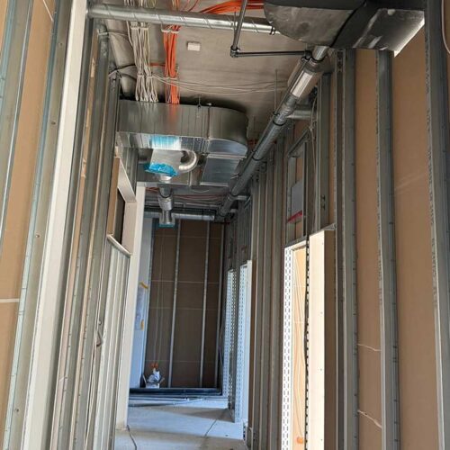 Ein Rohbauflur mit sichtbaren Metallträgern und farbigen Kabeln an der Decke