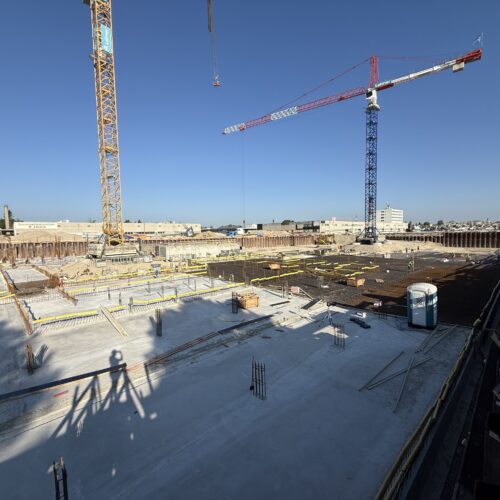 Großbaustelle mit Baukränen unter klarem blauem Himmel und leeren Fundamenten.