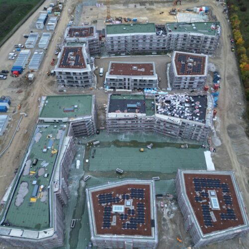 Luftaufnahme einer großen Baustelle mit mehreren teilweise fertiggestellten Gebäuden und grün-roten Dächern