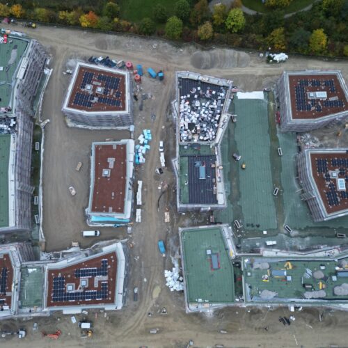 Luftaufnahme einer modernen Baustelle mit mehreren flachen Gebäuden und bunten Dächern