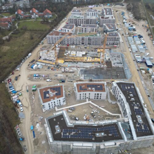 Luftaufnahme einer großen Baustelle mit mehreren weißen Gebäuden und roten Dächern