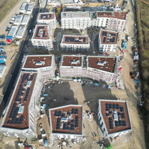 Mehrere moderne weiße Wohngebäude mit braunen Dächern und Solarpaneelen aus der Vogelperspektive