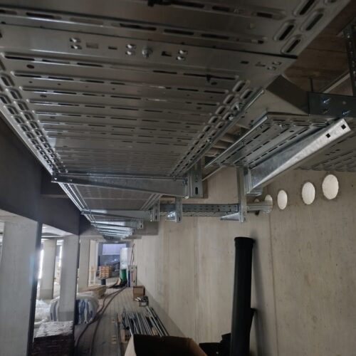 Mehrere  silberne  Kabeltrassen  verlaufen  an  einer  Betonwand  in  einem  Rohbau  entlang