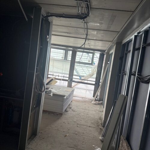 Ein  leerer  Baustellenflur  mit  Kabeln  an  der  Decke  und  gestapelten  Baumaterialien