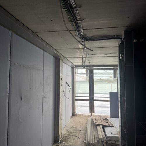 Ein  leerer  Rohbau  mit  grauen  Wänden  freiliegenden  Kabeln  und  Baustellenmaterialien
