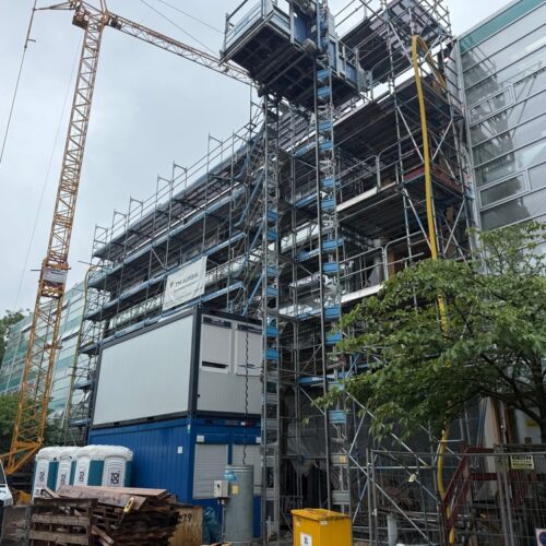 Eine  große  Baustelle  mit  Gerüsten  und  Kran  neben  einem  verglasten  modernen  Gebäude