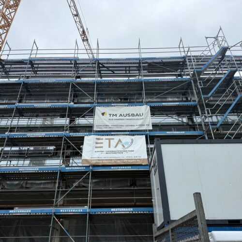 Mehrgeschossiges  Baugerüst  mit  Bauplanen  und  Werbebannern  vor  grauem  Himmel