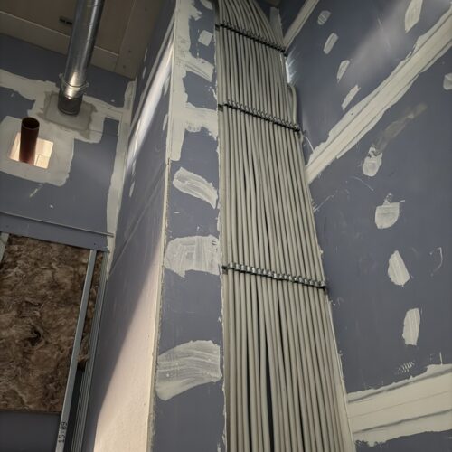 Das  Bild  zeigt  viele  weiße  Kabel,  die  ordentlich  an  einer  Wand  mit  grauen  Putzstellen  verlaufen