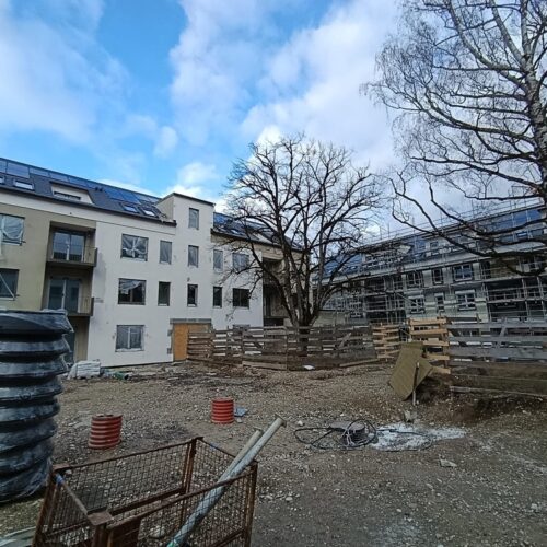 Eine  Baustelle  mit  zwei  mehrstöckigen  Gebäuden,  Bäumen  und  Bauzäunen  im  Vordergrund