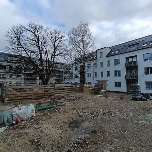 Zwei  mehrstöckige  Wohngebäude  stehen  neben  einer  Baustelle  mit  Kies  und  Baumaterialien