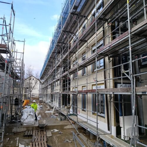 Eine  Baustelle  mit  Gerüsten,  mehreren  Etagen  und  zwei  Menschen  in  Warnkleidung