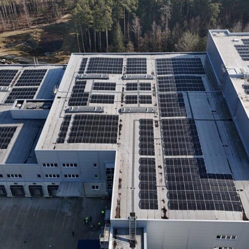 Lächelndes  graues  Fabrikdach  mit  schwarzen  Solarmodulen  und  Waldkante