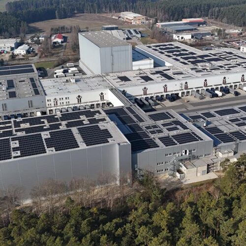 Luftbild  von  Industrieanlage  mit  Solardächern  in  Grau  zwischen  Wald  und  Straßen