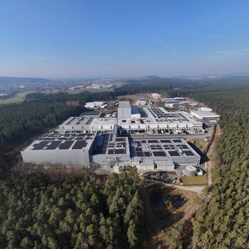 Luftaufnahme  eines  grauen  Industriekomplexes  mit  Solardächern  im  Wald