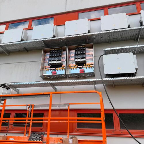 Oranger  Lift  vor  grauem  Gebäude  mit  roten  Fenstern  und  Schaltschränken